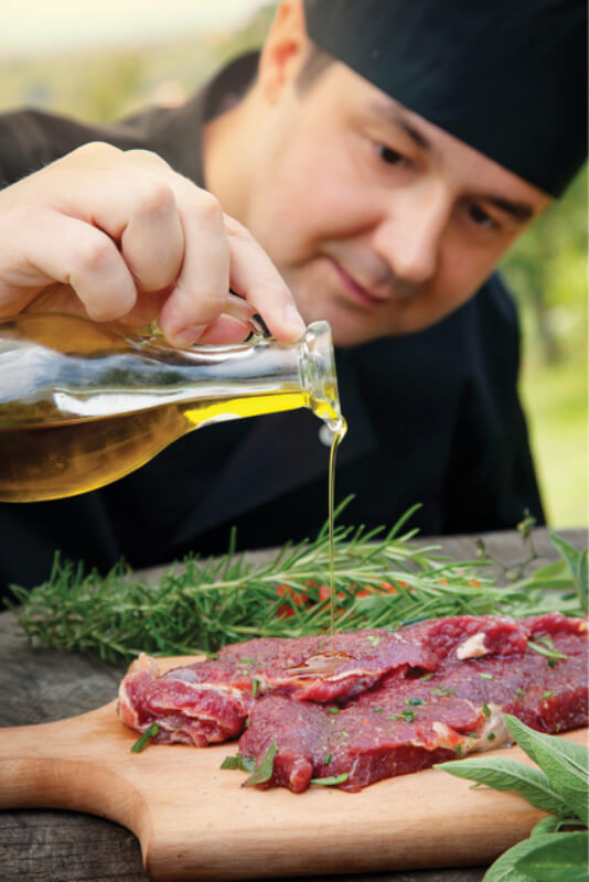 a chef pouring oil onto a raw steak