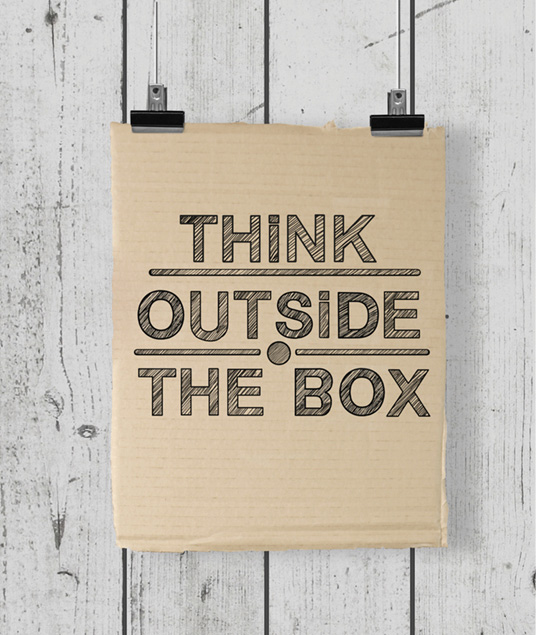 Cardboard sign with "think outside the box"written clipped onto a fence