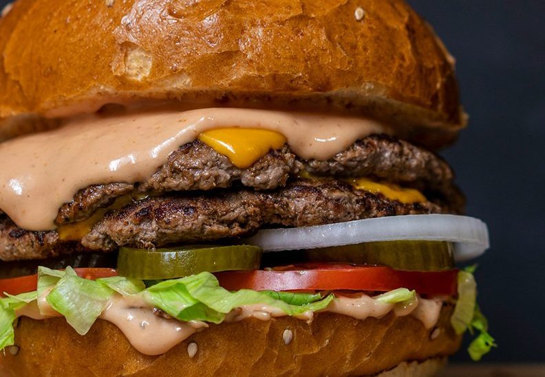 a burger with cheese onions gherkins tomato lettuce and burger sauce