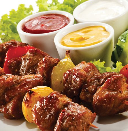 chicken skewers with multiple dipping suaces behind
